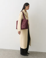 Person in a long coat carrying a tote bag with floral details.