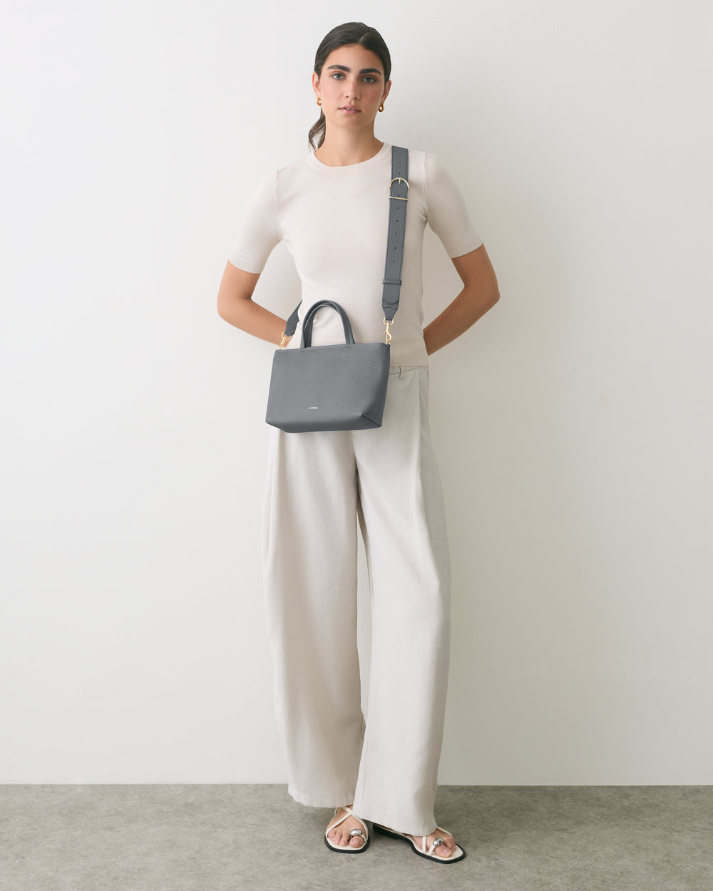 Person standing wearing a shirt and wide-leg pants, holding a shoulder bag.