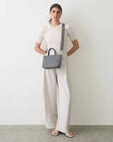 Person standing wearing a shirt and wide-leg pants, holding a shoulder bag.