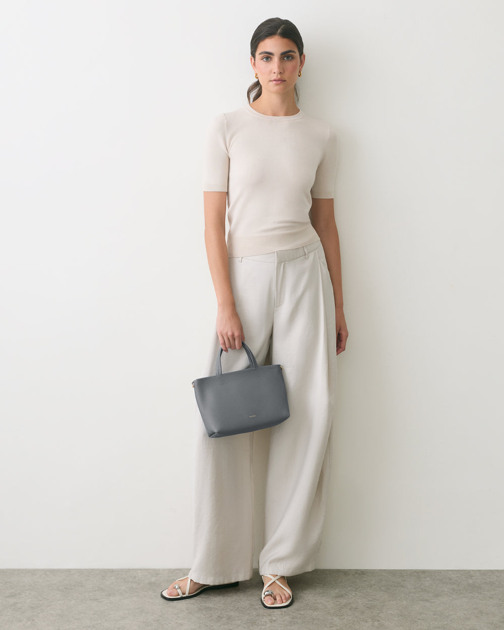 Person standing against wall holding small handbag wearing a short-sleeve top and wide-leg pants