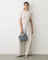Person standing against wall holding small handbag wearing a short-sleeve top and wide-leg pants