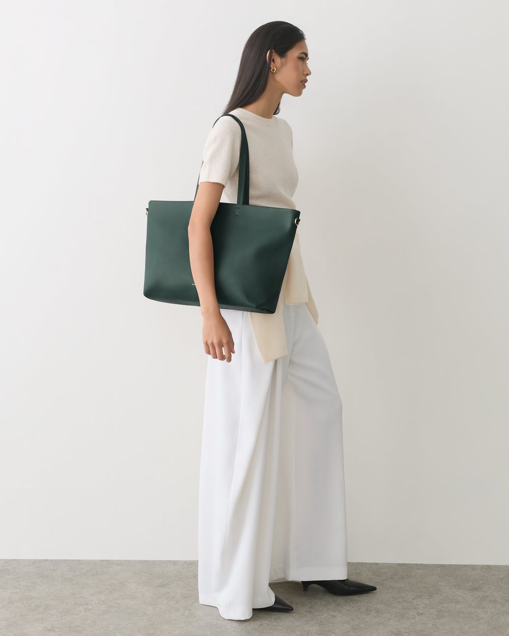 Person standing with shoulder bag wearing long pants and a top.