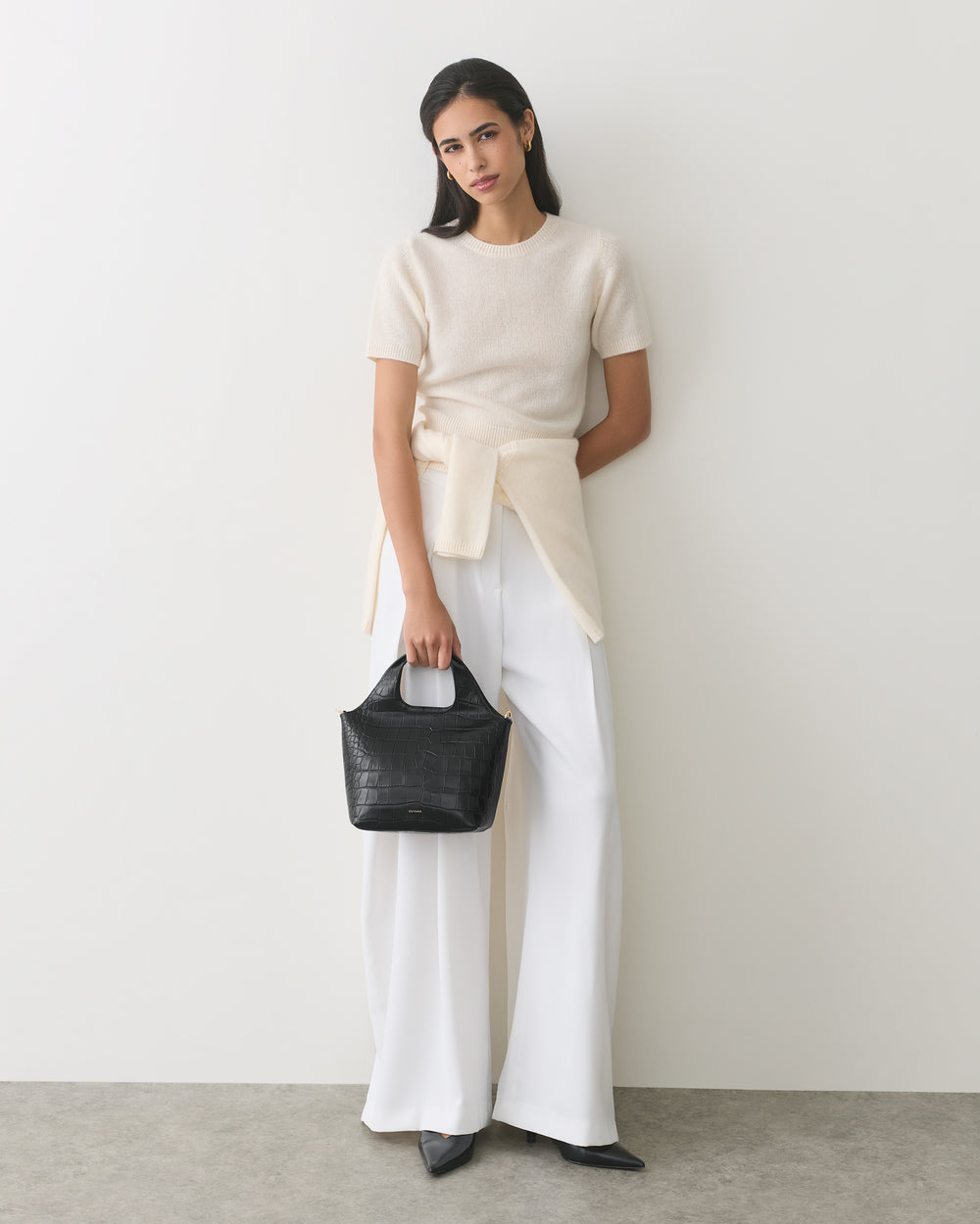 Woman in white outfit holding croc-embossed leather handbag.