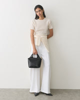 Woman in white outfit holding croc-embossed leather handbag.