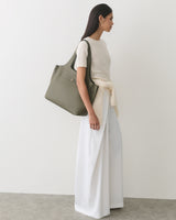 Person in sleeveless top and wide-leg pants holding a large shoulder bag.