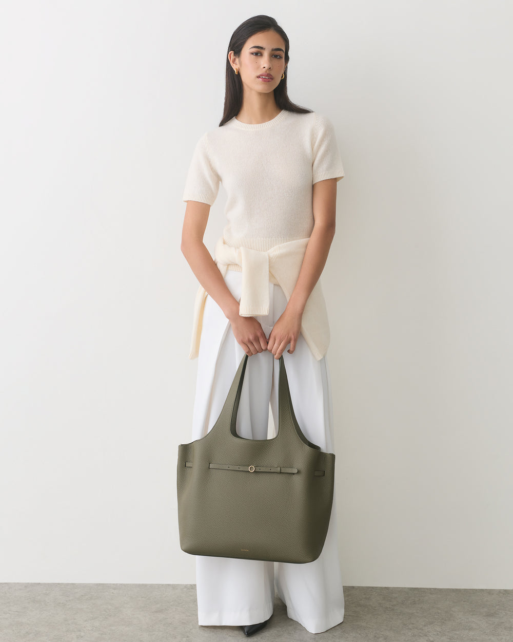 Person holding a large tote bag, wearing a top and wide-legged pants.