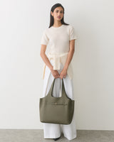 Person holding a large tote bag, wearing a top and wide-legged pants.