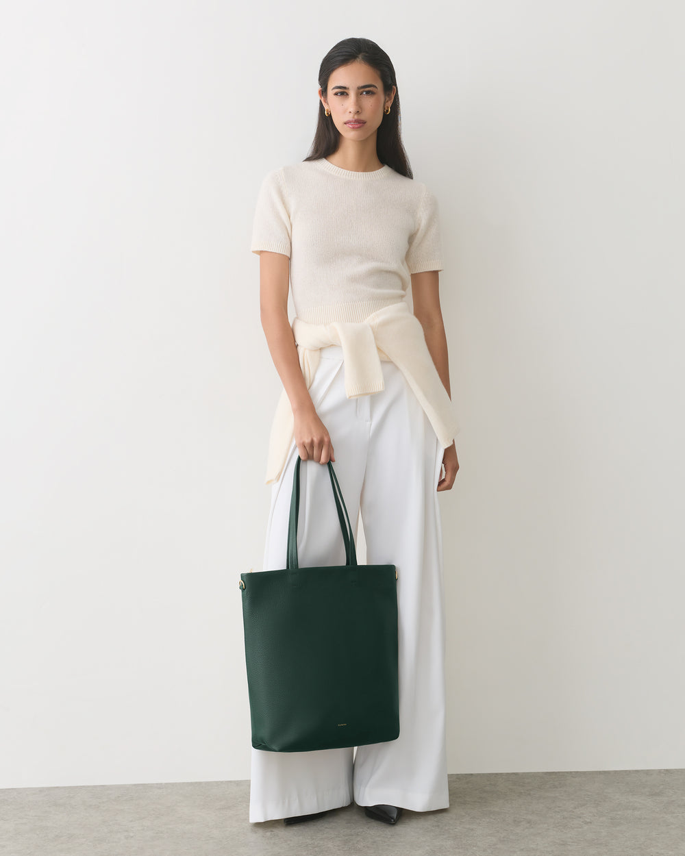 Woman in white outfit holding a dark tote bag.