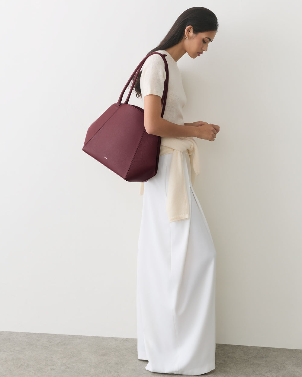 Person stands sideways with large handbag, wearing a long skirt and top.