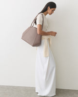 Person standing sideways holding a handbag, wearing a long skirt and a top with tied sweater.