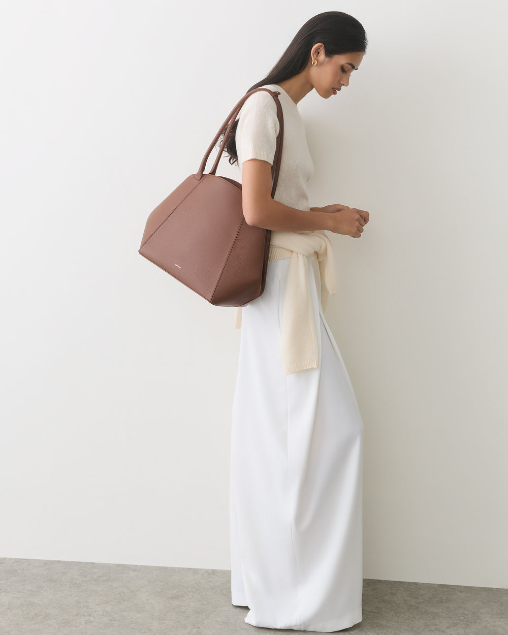 Person in light sweater and pants, holding a large bag on their shoulder.
