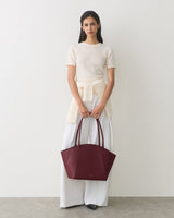 Person holding large handbag wearing a short-sleeve top with tied sweater and wide-leg pants.