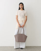 Person holds handbag wearing short-sleeve top, long pants, and sweater tied at waist.