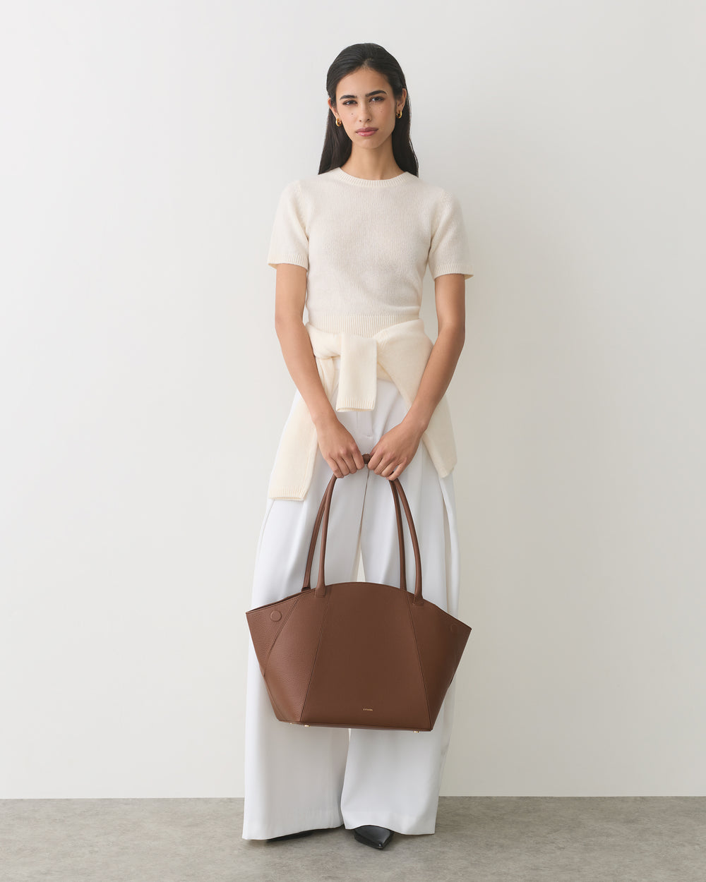 Person holding a large handbag, wearing a short-sleeved top and wide-leg pants.
