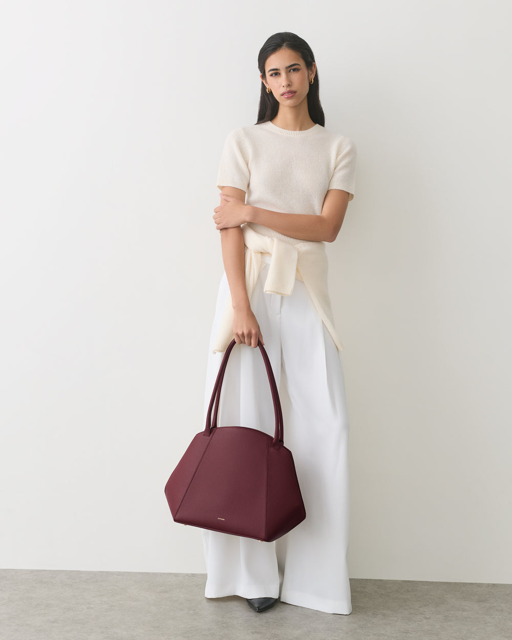 Woman holding a handbag, wearing a top and wide-legged pants.