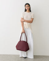 Woman holding a handbag, wearing a top and wide-legged pants.
