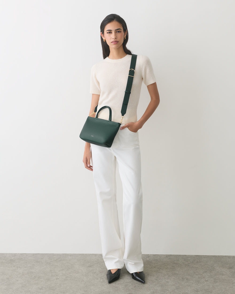 Person in a plain shirt and pants holding a handbag over the shoulder.