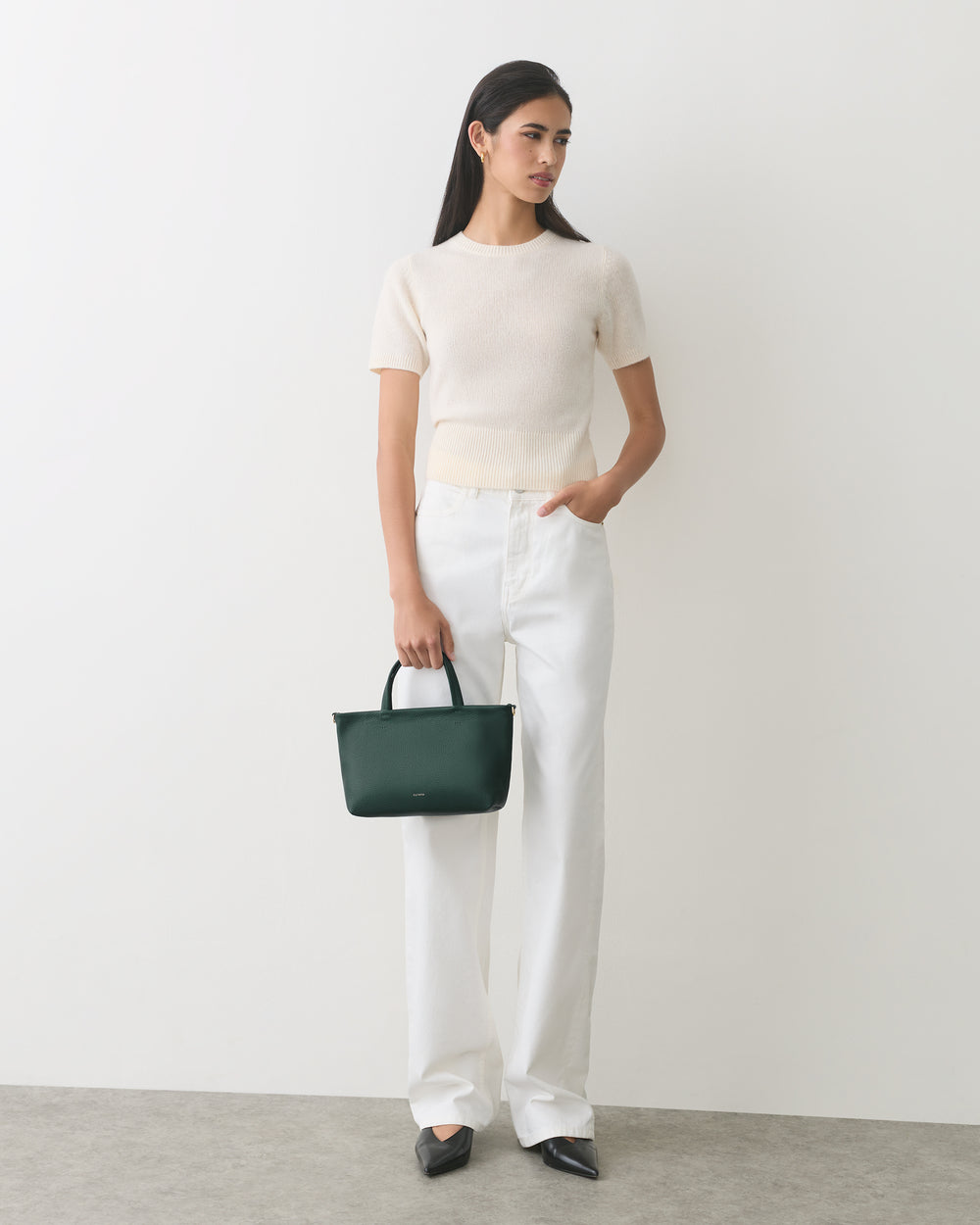 Person standing, holding a handbag, wearing a short-sleeve top and long pants.