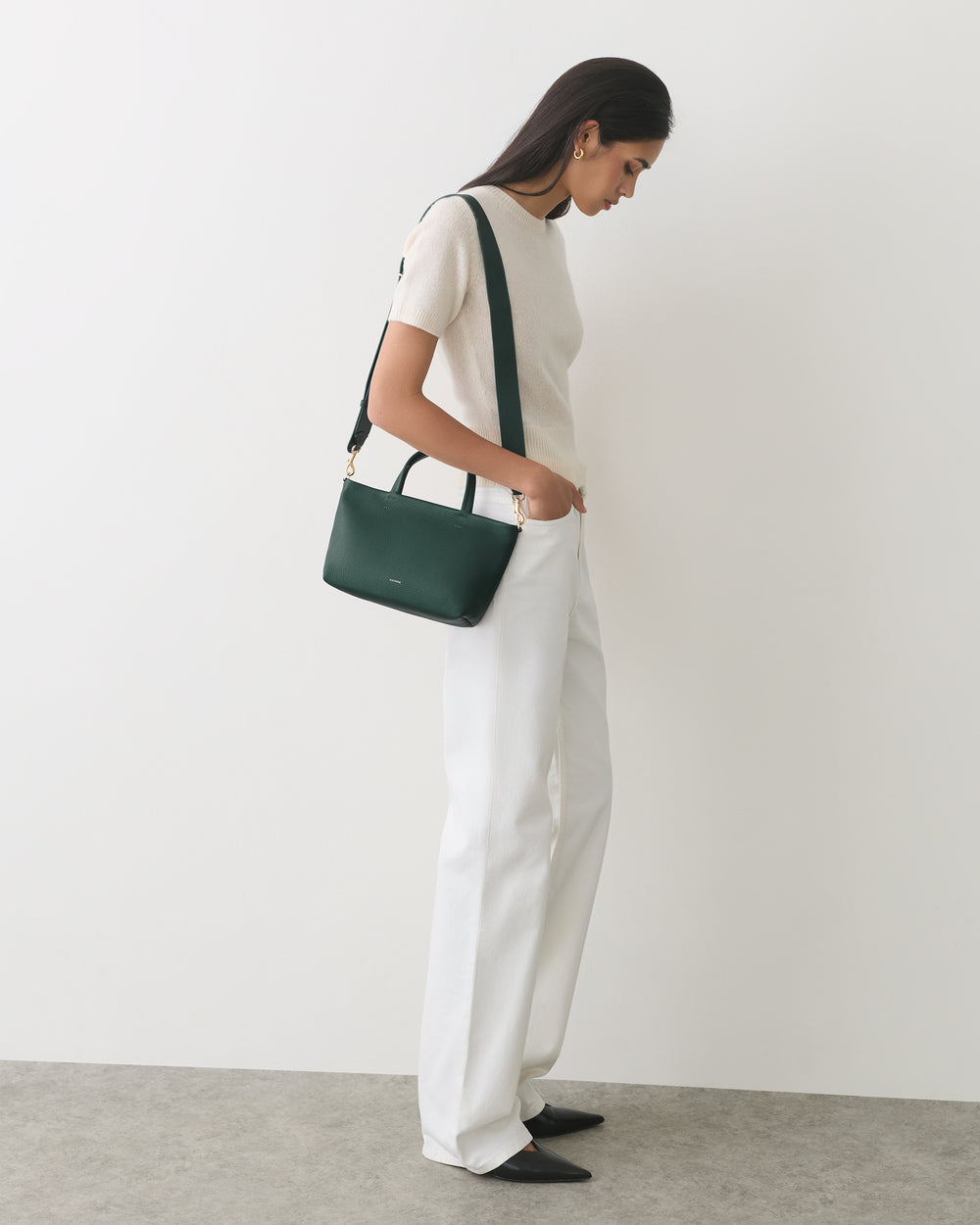 Person standing, holding a shoulder bag, wearing a short-sleeve top and pants.