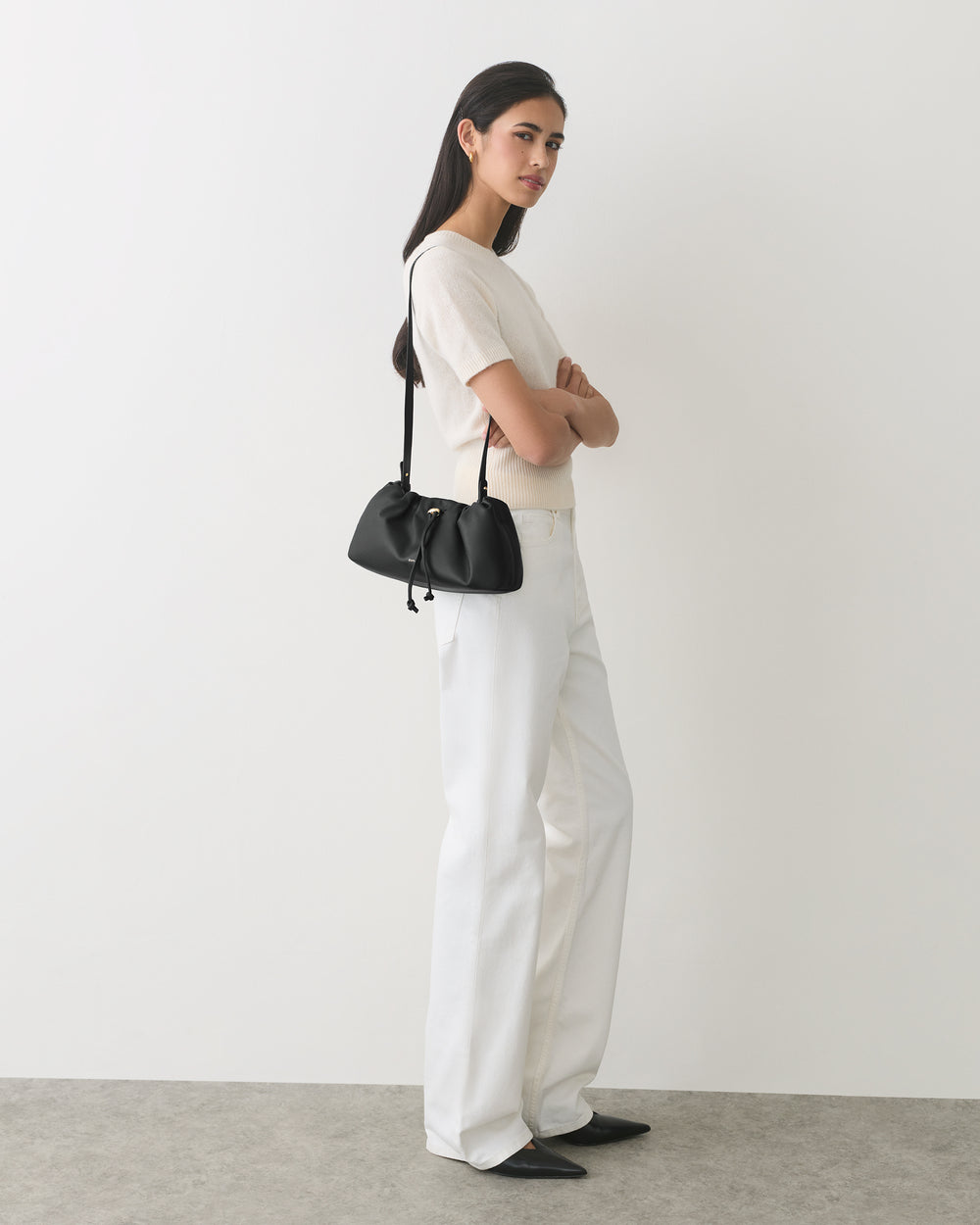 Person standing, arms crossed, wearing a shirt, pants, and holding a shoulder bag.