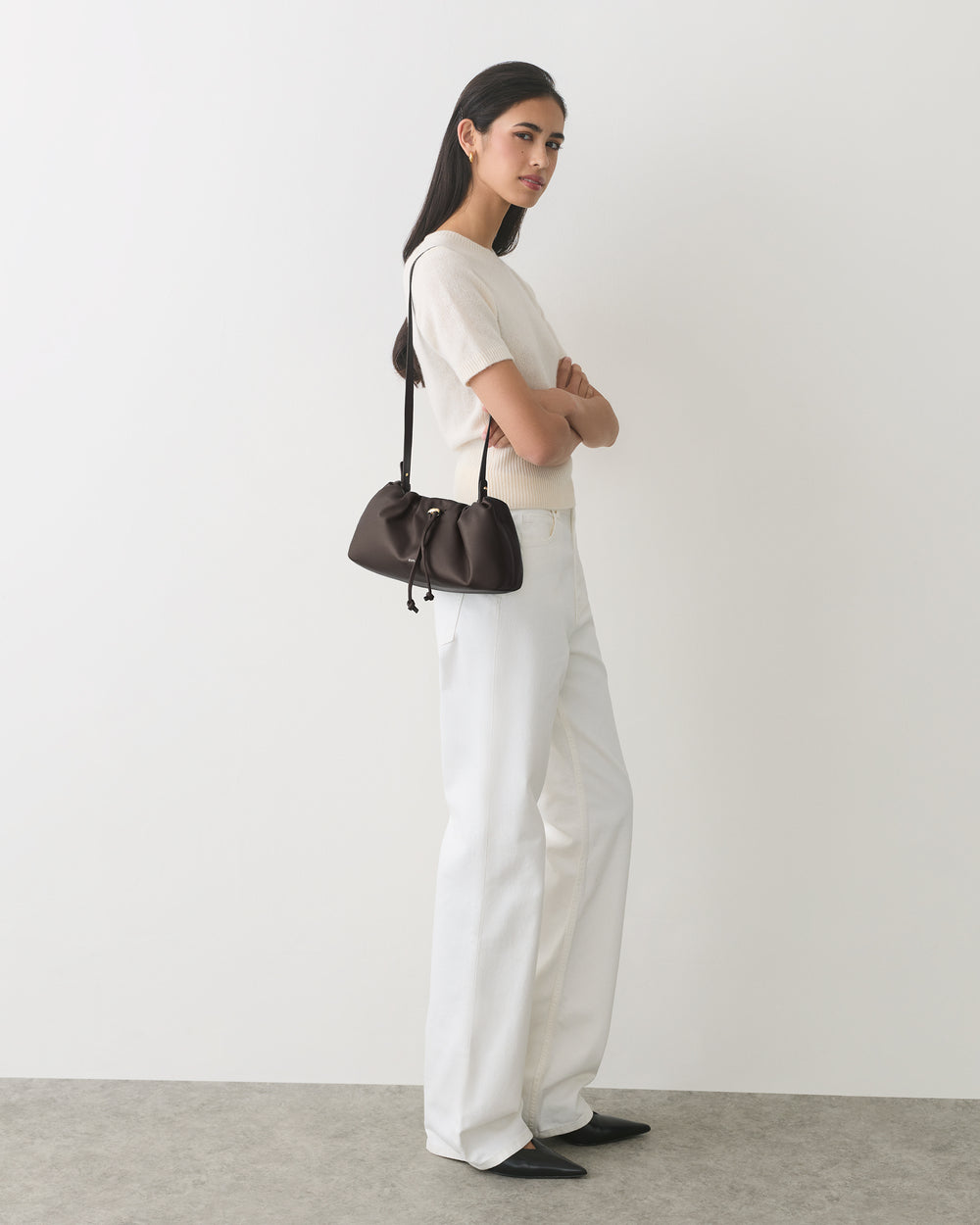 Person posing with a small shoulder bag wearing a short-sleeve top and wide-leg pants.