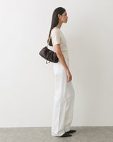 Person standing sideways wearing a short sleeve top, trousers, small shoulder bag, and shoes.