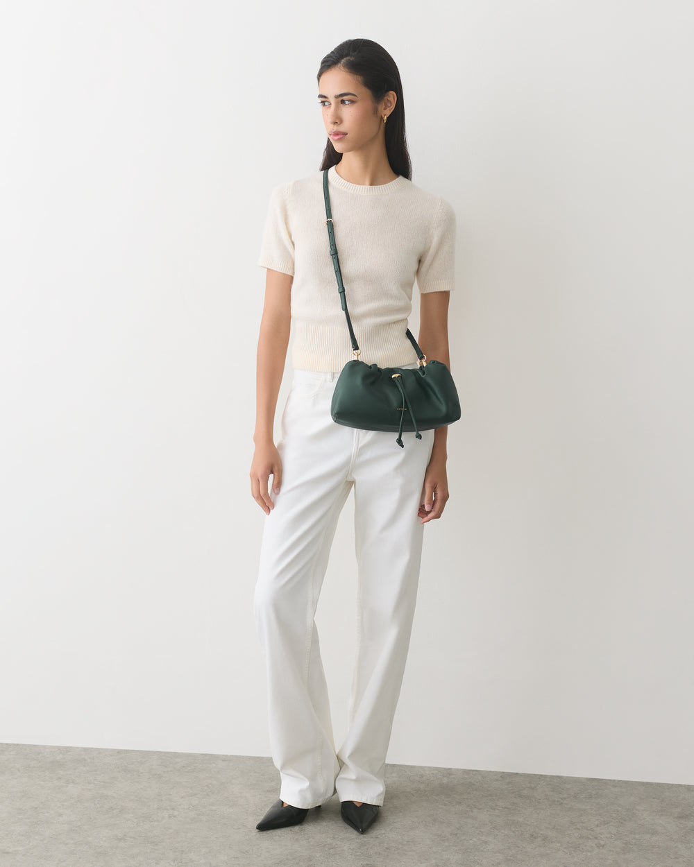 Person in short-sleeve top and trousers holding a shoulder bag.