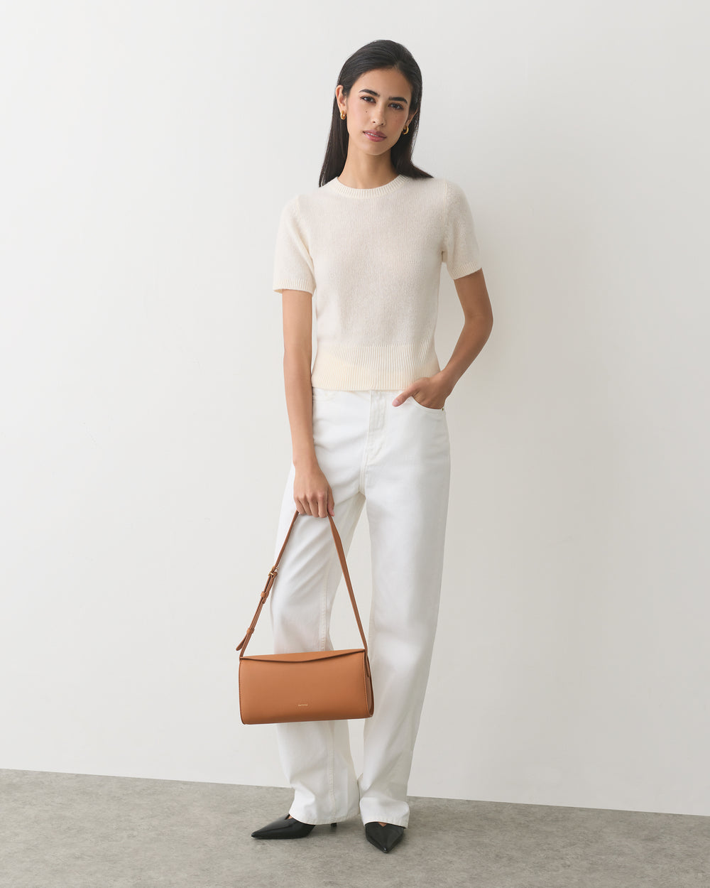 Person wearing a short-sleeve top and pants, holding a shoulder bag.