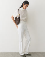 Person posing with a shoulder bag, wearing a short-sleeve top and pants.