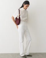 Person in a top and pants, holding a shoulder bag while standing against a plain background.