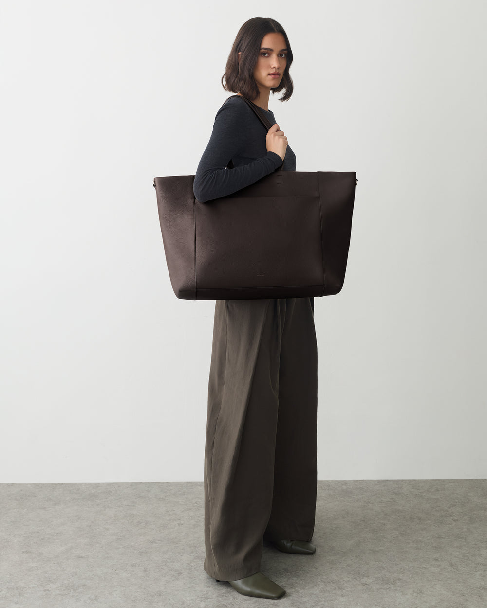 Person carrying a large tote bag stands on a plain background.
