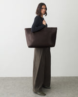 Person carrying a large tote bag stands on a plain background.