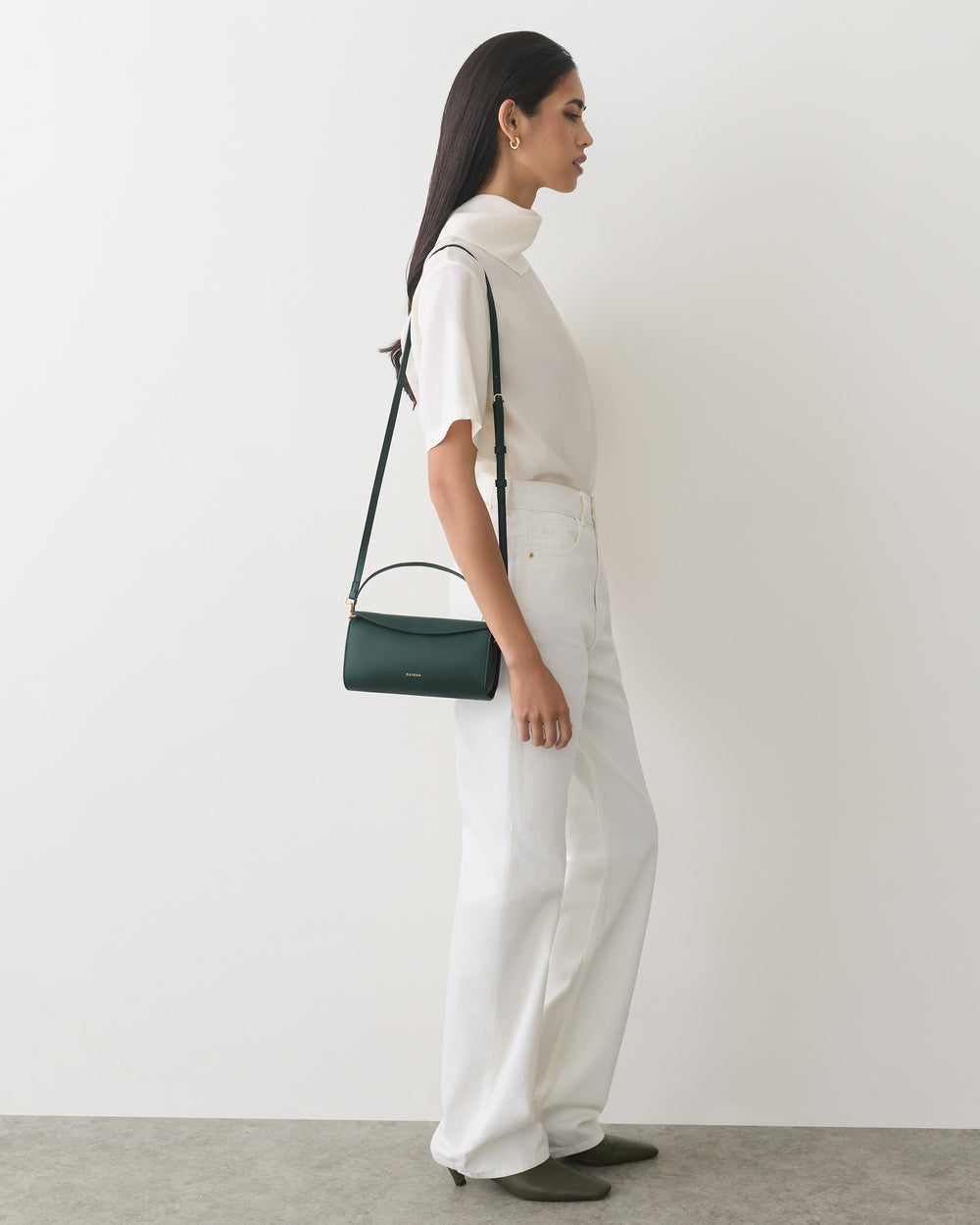 Person in side profile wearing a top and pants, holding a shoulder bag.