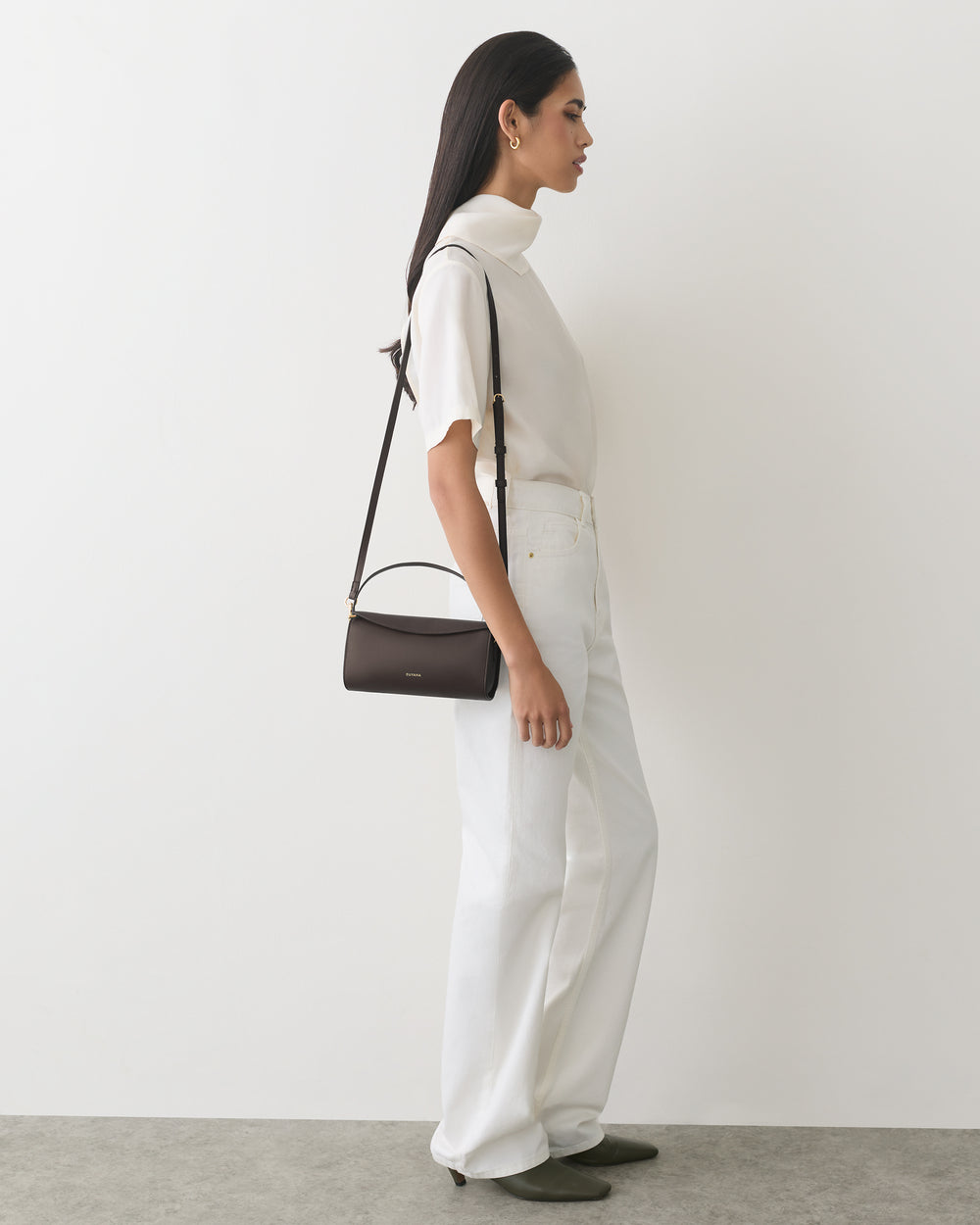 Person in a turtleneck and pants with a shoulder bag, standing sideways.