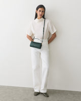 Person wearing white outfit with a small handbag, standing against a plain wall.
