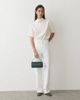 Person standing with a small handbag, wearing a short-sleeve top and long pants