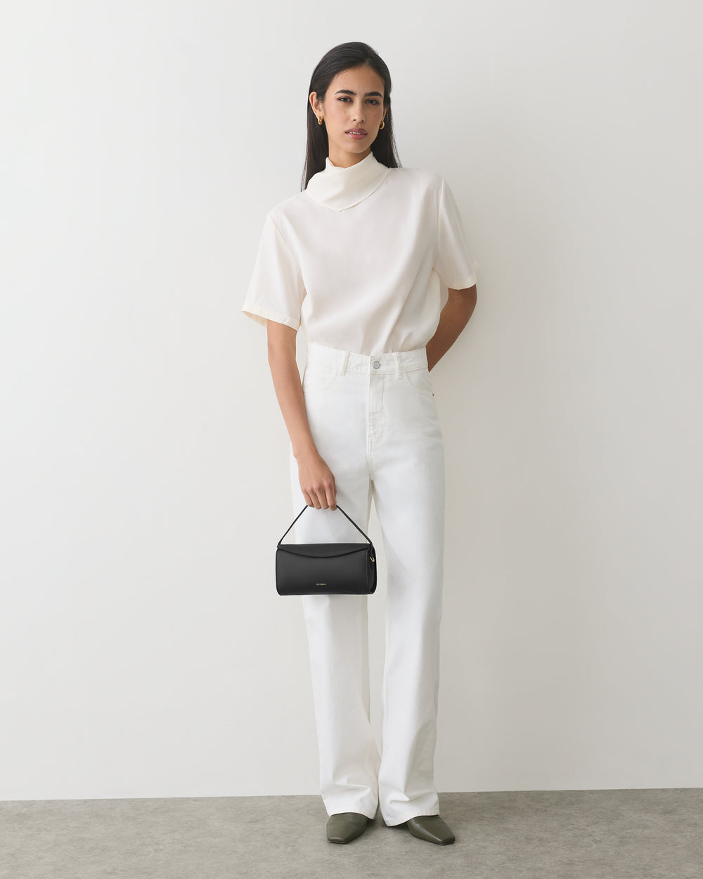 Person in t-shirt and pants holding a small handbag.