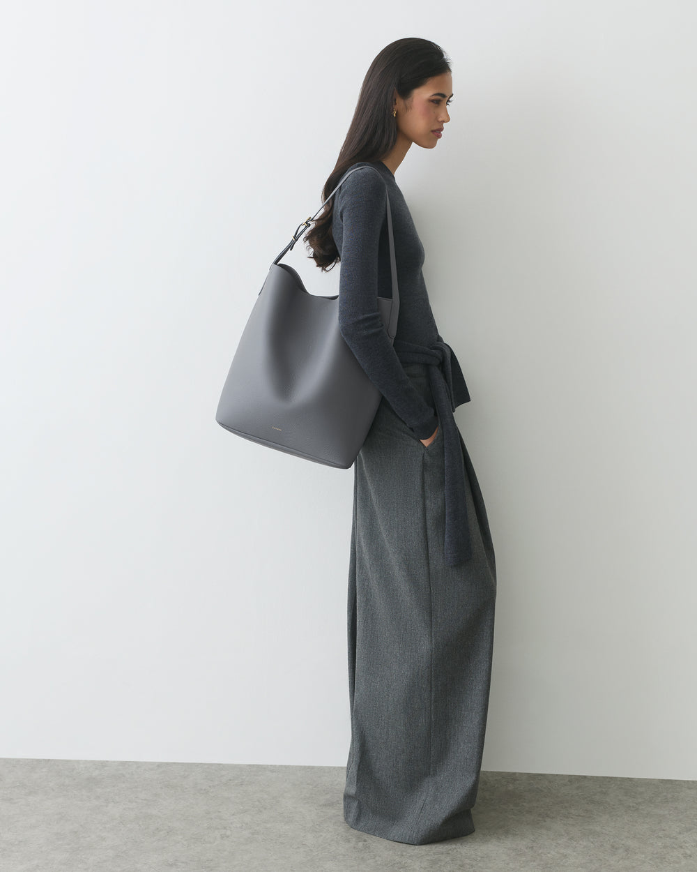 Person in trousers and a sweater, wearing a large shoulder bag.