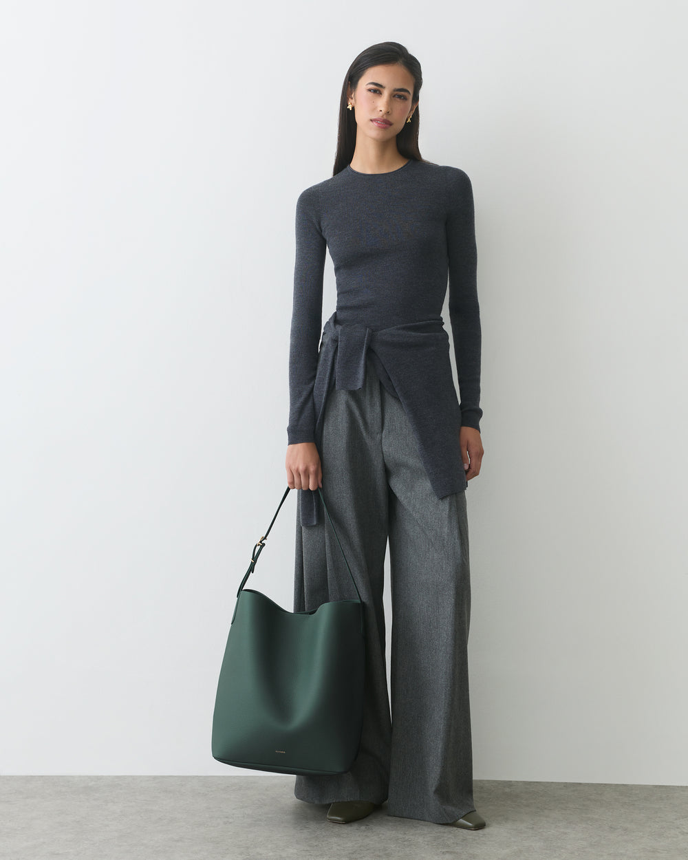 Person wearing a long-sleeve top and wide-leg pants holds a large handbag.