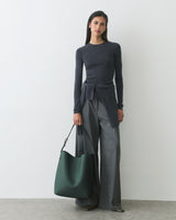 Person wearing a long-sleeve top and wide-leg pants holds a large handbag.