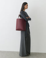 Person standing with arms crossed, holding large tote bag, wearing long pants and long-sleeve top