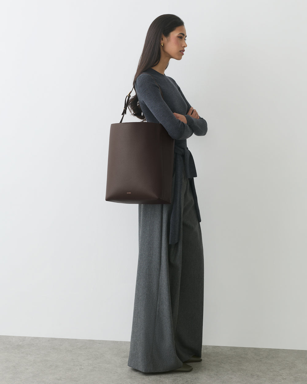 Woman standing with large handbag, wearing long-sleeve top and wide-leg pants.