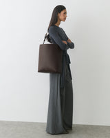 Woman standing with large handbag, wearing long-sleeve top and wide-leg pants.