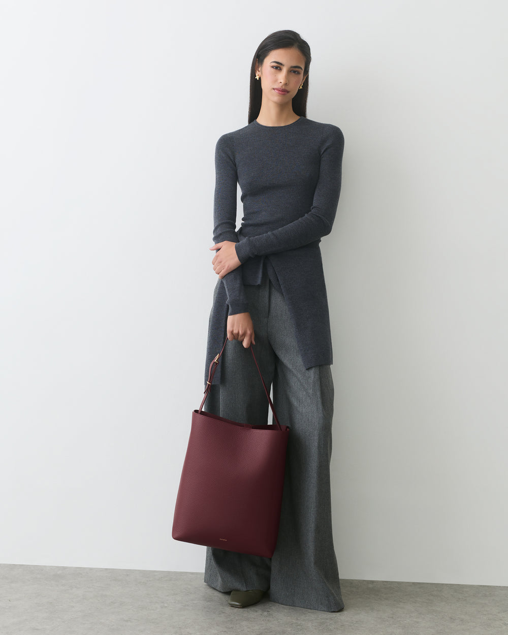 Person standing with a shoulder bag, wearing a long-sleeve top and wide-leg pants.