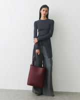 Person standing with a shoulder bag, wearing a long-sleeve top and wide-leg pants.