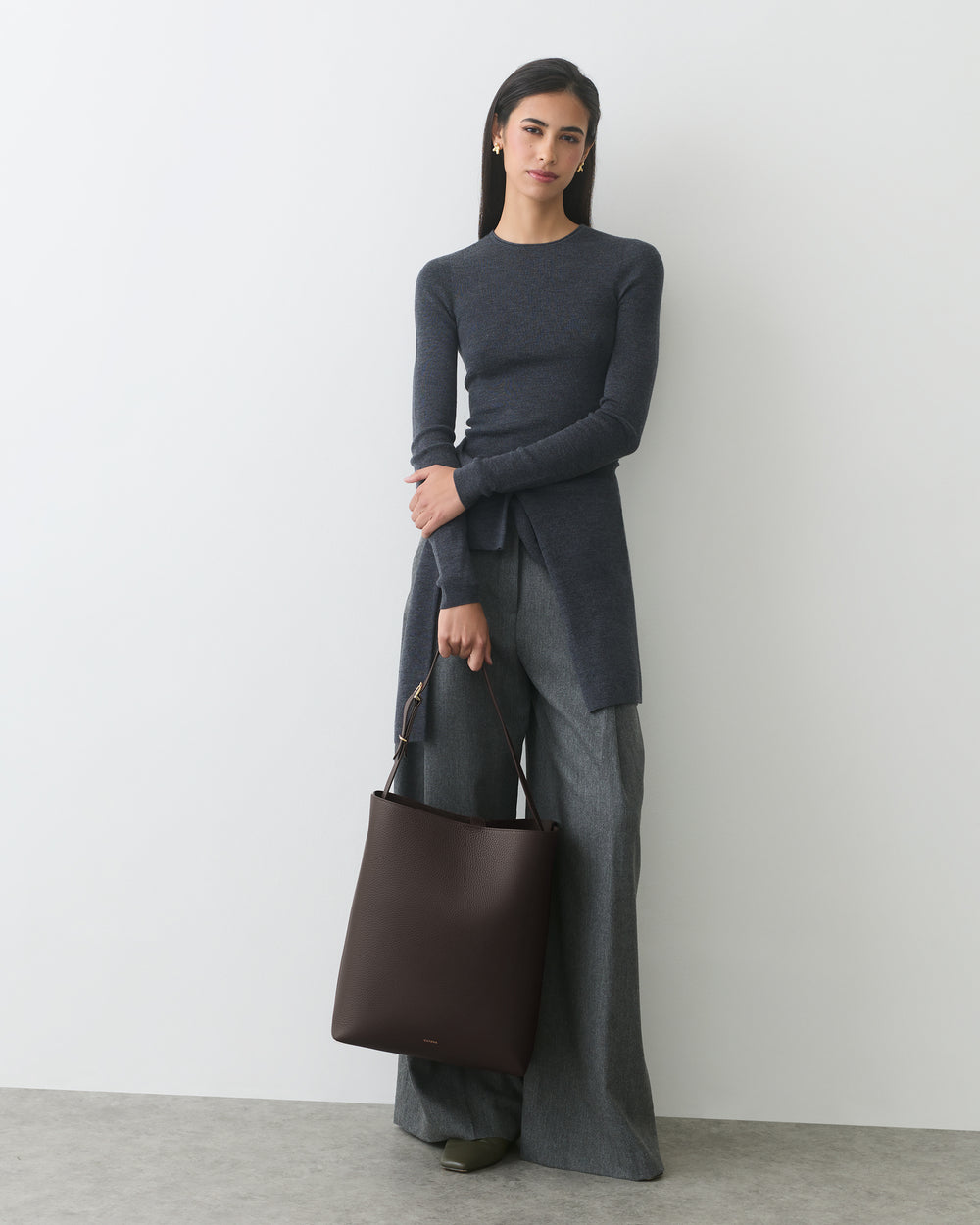 Woman in long-sleeve top and wide-leg pants holding a shoulder bag.