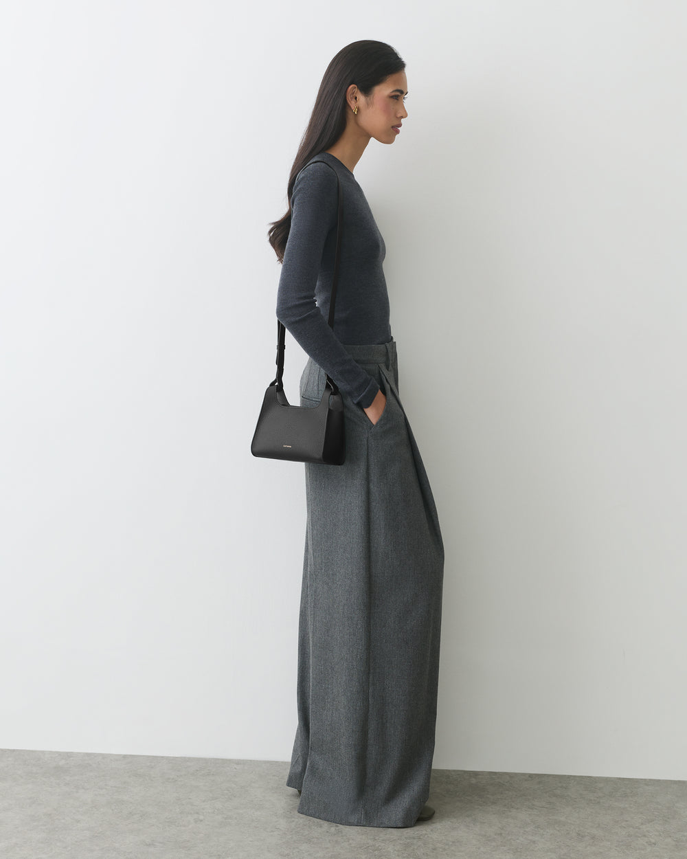 Person in long-sleeve top and wide-leg pants holding a small shoulder bag.