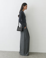 Person in long-sleeve top and wide-leg pants holding a small shoulder bag.