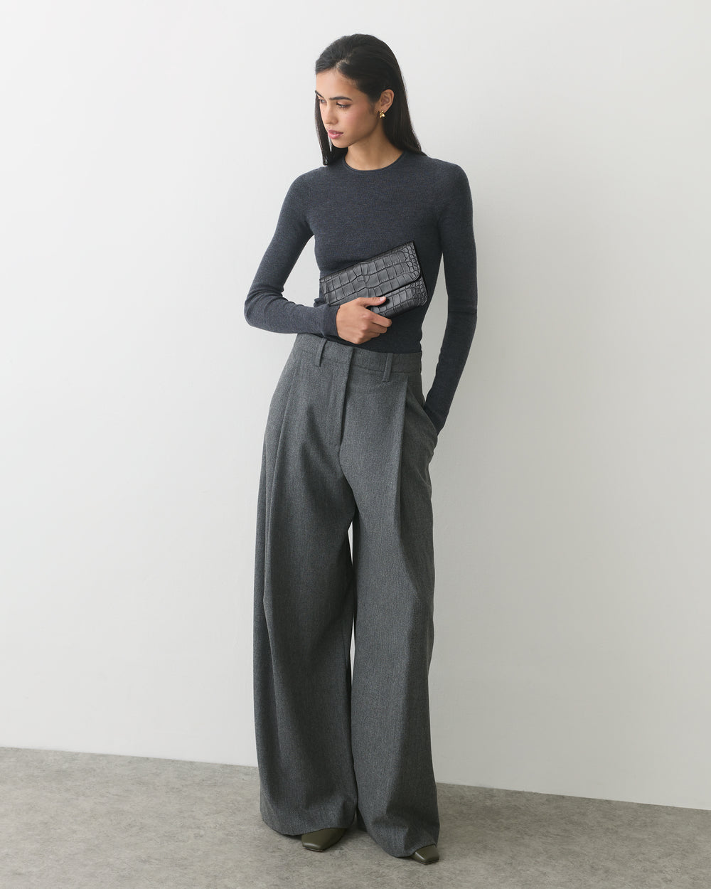 Person in long-sleeve top and wide-leg pants holding a croc-embossed leather clutch.