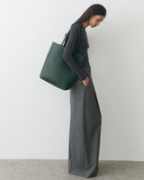 Person stands sideways holding tote bag and wearing long pants.
